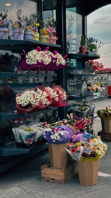 A display of fresh floral arrangements and bouquets on shelves and the ground outside Hatton Florist's shop, featuring a variety of flowers including white daisies, pink lilies, purple irises, and mul